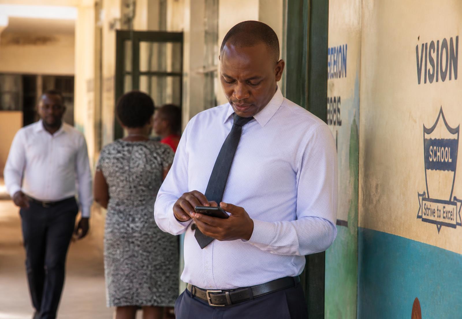 A teacher tapping to clock in on his phone at the school entrance.